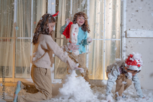 Cuadro en lienzo Three kids dressed in festive Christmas clothing enjoy playing with artificial snow on a cozy balcony, capturing the warmth and fun of the holiday season at home in a joyful moment