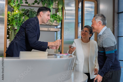 Cuadro en lienzo Friendly concierge assisting senior couple at modern hotel reception desk, providing direction with warm service and welcoming hospitality in a stylish urban environment
