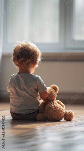 A young child sits near a window, gently hugging a teddy bear. The warm natural light creates a tender and comforting atmosphere, evoking feelings of security and love. AI generated.