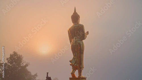 time lapse Standing majestically against a hazy sunrise sky, the Golden Buddha watches over a sea of mist covering Nan Province. The harmonious blend of golden sculpture, fog, and dawn light