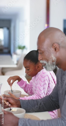 Vertical video: African American father and daughter at counter stirring bowls and eating for meal