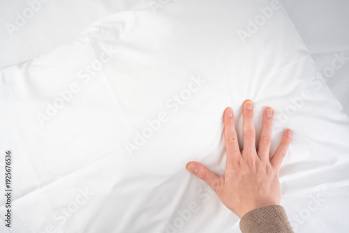 A person's hand gently presses into a fluffy white pillow on clean bedding
