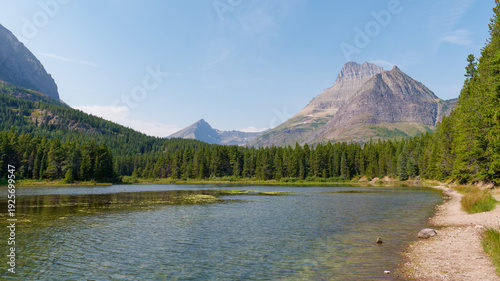 Photos Serene mountain lake surrounded by pine forests and rugged peaks in Glacier Nati