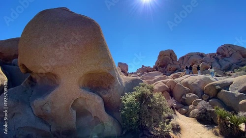 💀 Skull Rock Discovery: Adventure and Scale in Joshua Tree. Happy tourists are seen on giant boulders in the distance under a sunny blue sky. Iconic desert landscape and adventure vibe in Joshua Tree