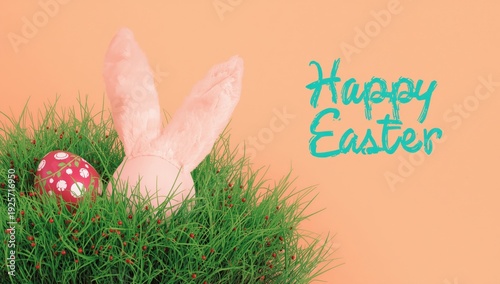 Pink bunny ears in grass with red Easter egg and Happy Easter text green grass white flowers