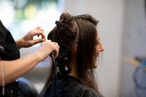 Calm atmosphere during hair styling process, Closeup of stylist working on damp hair in salon, Candid scene showing stylist carefully braiding damp hair with warm lighting