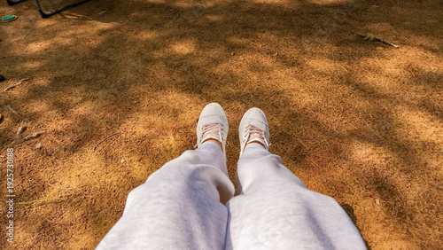 Obraz na plátne Person wearing white sneakers and gray sweatpants sitting on brown ground with s
