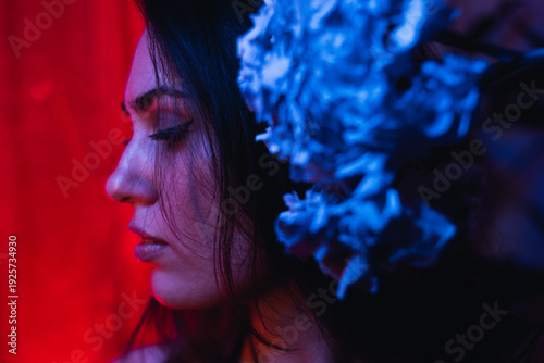 Moody portrait of a woman in colorful lighting with flowers, emotional expression in red, blue, and teal tones