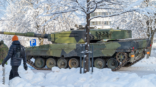 Leopard 2A4 main battle tank in winter conditions. Heavy armored military vehicle on a snowy street. Arctic military equipment and urban background.