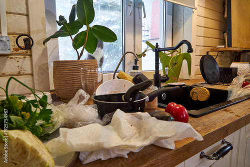 Foto Messy modern kitchen after cooking with dirty dishes, fresh vegetables and cluttered countertop