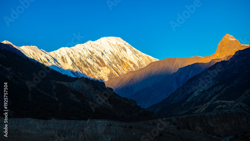 Billede på lærred Sunrise alpenglow lights a snowcapped Himalayan peak with deep blue shadows in the valley, Annapurna region of Nepal