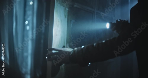 Closeup, handheld shot on woman's hand holding flashlight and quickly entering creepy room 