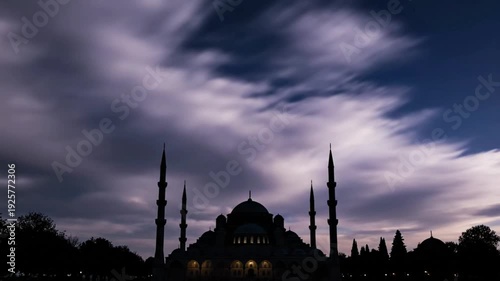 Silhouette of a grand mosque with minarets against a dramatic, streaky cloudscape at dusk, long exposure.