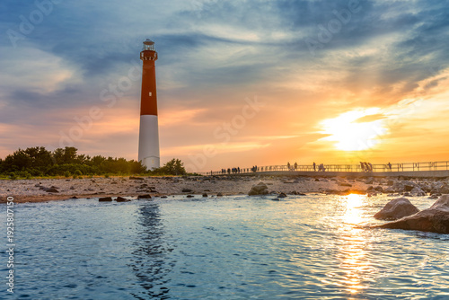 Barnegat Lighthouse at sunset. Barnegat Lighthouse is a historic lighthouse located in Barnegat Lighthouse State Park in New Jersey. Numerous unidentifiable tourists enjoy the warm end of the day.