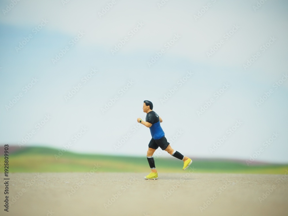 Obraz premium Mini toy of action figure at table with blurred background. Miniature photography concept. Runner at outdoor conceptual design. Young man running at outdoor.
