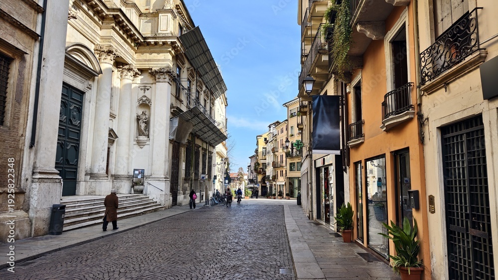 Obraz premium The street in the old town is paved with paving stones and tiled sidewalks. There are historic buildings with storefronts and balconies nearby, as well as outdoor cafes with awnings. Sunny winter
