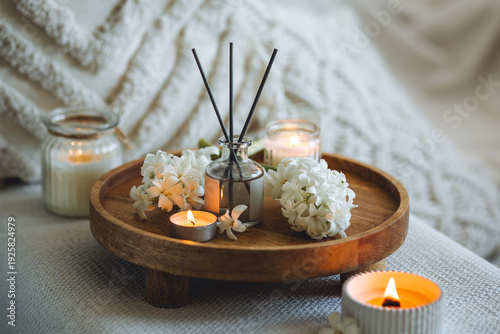Aroma diffuser, burning candle, blooming hyacinth flowers and perfume on wooden bamboo tray. Cozy home decor, hygge and aromatherapy concept. Comfortable atmosphere, spring delicious fresh smell