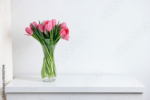 Bouquet of pink tulips in vase on chest of drawers near white wall indoors. Space for text
