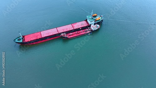 Aerial view of a cargo ship and tanker in open water. A large red and black cargo vessel positioned next to a smaller red tanker ship on calm green water.
