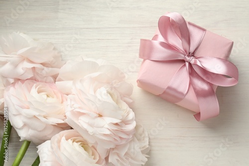 Beautiful flowers and gift on white wooden table, flat lay