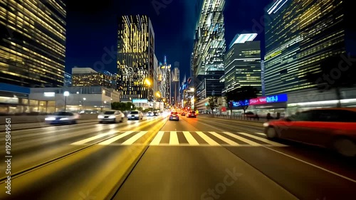 A busy city road at night, with illuminated high-rises and blurred car lights creating motion