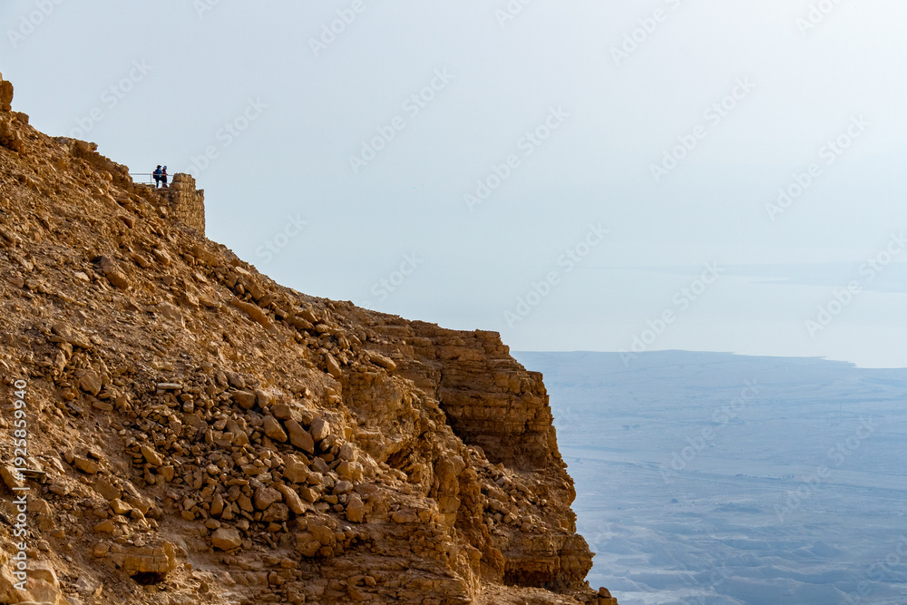 Fototapeta premium Ancient ruins of Masada fortress on a mountain top in the Judean Desert, Israel, overlooking the Dead Sea under a clear spring sky. Historical archaeological site and famous landmark at sunrise.