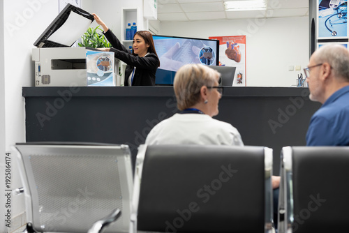 Quadro em tela Asian receptionist using copier and scanning machine at front desk of modern healthcare facility