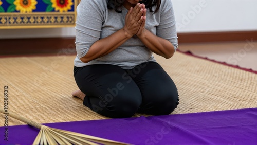 Devout Filipina woman kneeling on woven mat, hands clasped tightly in prayer, foreground shows texture of purple altar cloth and dried palm fronds