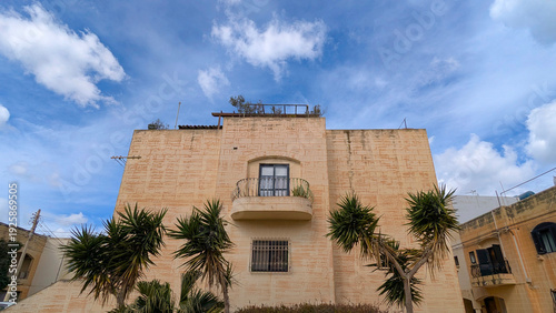 Wallpaper Mural Natural limestone apartment facade with small curved balcony framed by palm trees, bright calm Malta street scene Torontodigital.ca