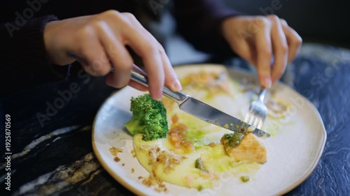 Wallpaper Mural Close up of hands using knife and fork to cut a salmon fillet served with broccoli and sauce Torontodigital.ca