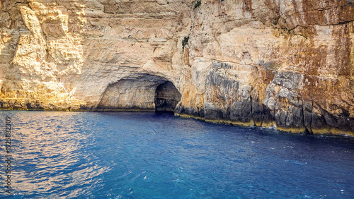 Rocky Sea Cave on Mediterranean Coast with Crystal Clear Blue Water and Dramatic Cliffs.
Natural limestone cave carved by the sea, illuminated by warm sunlight and surrounded by deep turquoise water.
