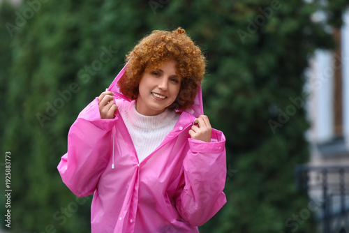 Beautiful young woman in pink raincoat outdoors