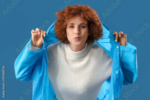 Fotografi Young woman in blue raincoat blowing kiss on color background