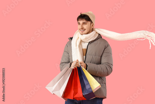 Young man in winter clothes with shopping bags on pink background