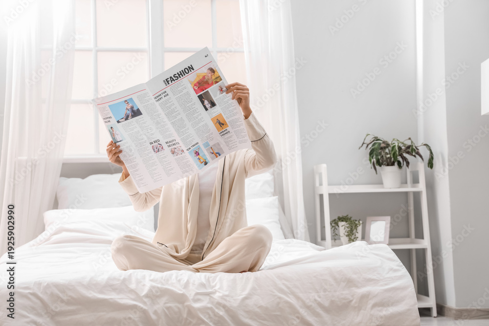 © Pixel-Shot - Young woman with newspaper sitting in bedroom