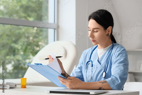 Tattooed female doctor writing at table in clinic