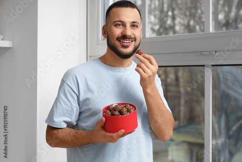 Young man eating chocolate candy in kitchen