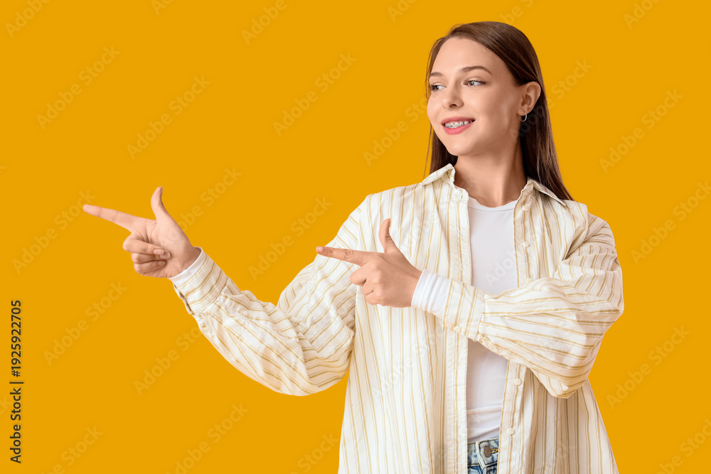 Naklejka premium Beautiful happy young woman pointing at something on yellow background