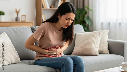Woman suffering Stomach pain: A person sits hunched over on a couch, clutching their stomach with an expression of distress, symbolizing discomfort and internal struggle.