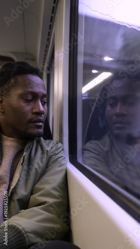 A black man looking out of the window of a train to London, contemplating life