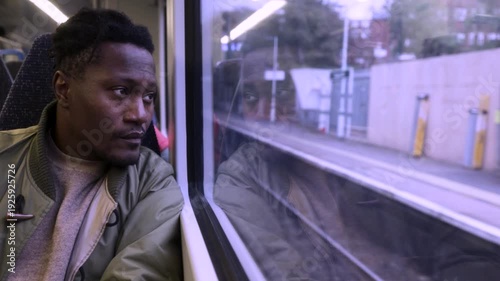 A black man looking out of the window of a train to London, contemplating life