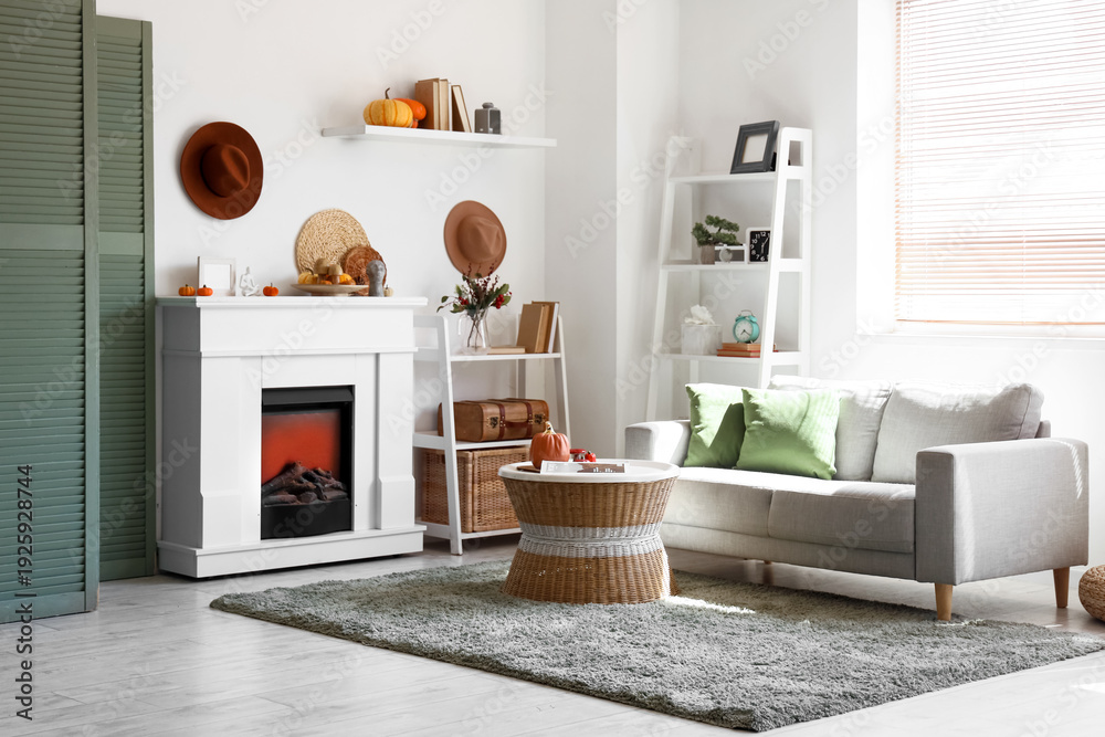 Fototapeta premium Stylish living room with white fireplace, soft sofa, coffee table and pumpkins. Autumn concept