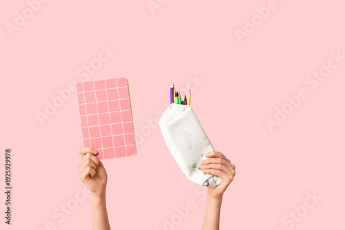 Foto Female hands holding notebook and pencil case with stationery on pink background