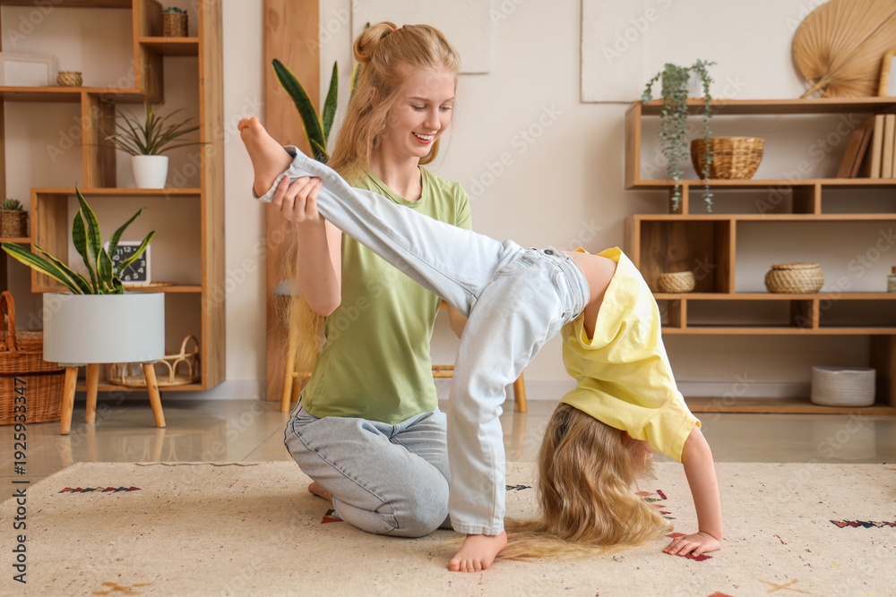 Fototapeta premium Beautiful young sporty woman with her little daughter practising yoga in living room