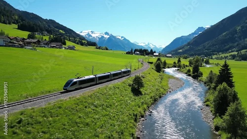 Modern Train Traveling Through Scenic Alpine Valley with River and Snow-Capped Mountains