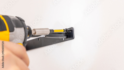 Wallpaper Mural Mans hands adjusting black metal shelf bracket on white wall with yellow cordless drill nearby. Home improvement, bracket fine-tuning, DIY alignment correction, installation adjustment. Torontodigital.ca
