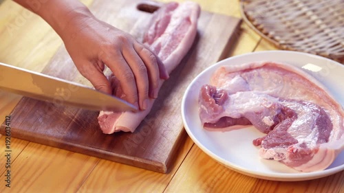 Hands slicing fresh raw pork belly on wooden cutting board in home kitchen, food preparation process for cooking meal, close up culinary preparation and ingredient handling