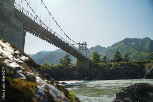 a bridge crossing seething mountains and a river, a suspension bridge with people walking on it.