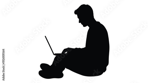 A silhouetted figure sits cross legged intently working on a laptop computer