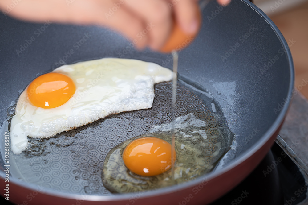 Fototapeta premium Hand cracking a fresh egg into a frying pan for fried egg